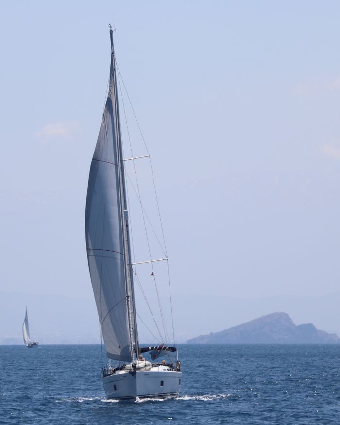 A sailboat navigates the open sea under a clear blue sky, capturing peaceful maritime travel.
