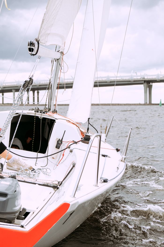 A sleek sailboat navigating the waves with a bridge visible in the background.