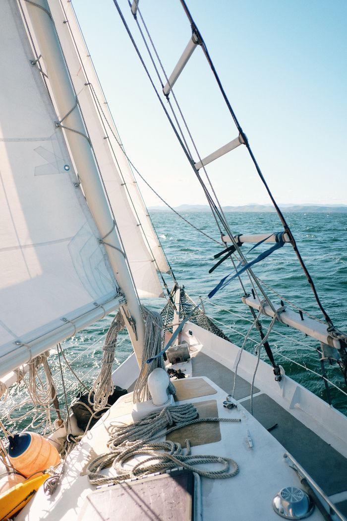 Home Experience the tranquility of sailing on a sunny day with this serene image of a sailboat cutting through the open sea.
