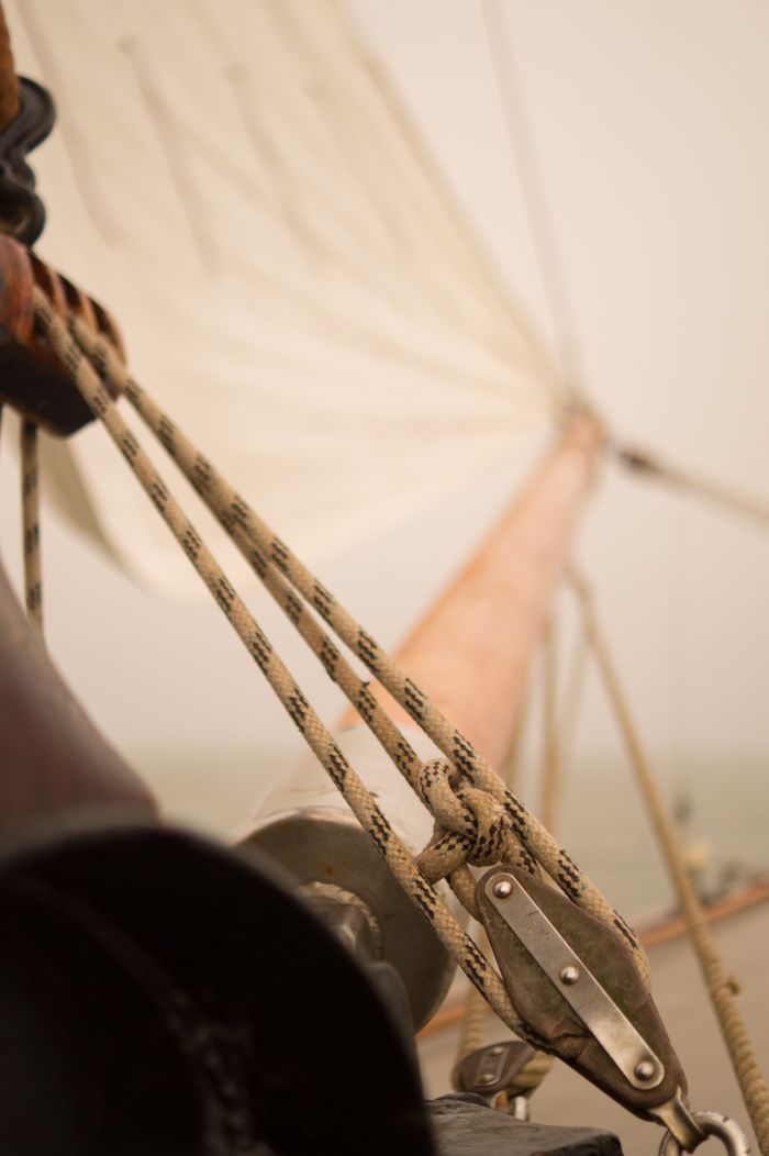 Detailed view of sailboat rigging with ropes, masts, and a sail in the background.